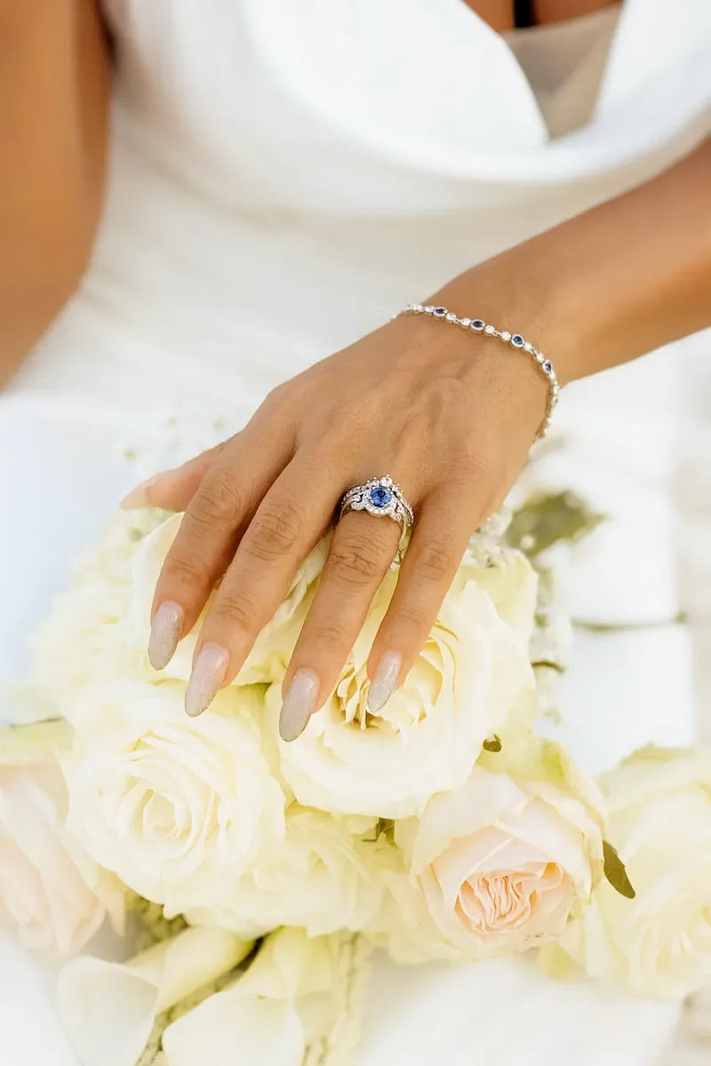 Anillo de compromiso de zafiro con orla de diamantes en la mano de la novia sobre ramo de rosas