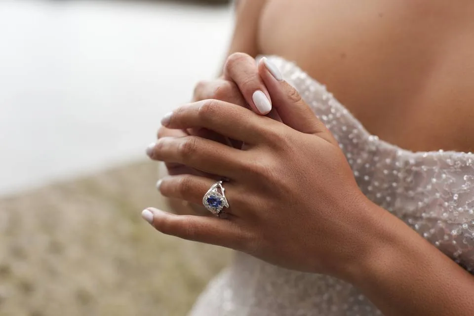 Novia con anillo de compromiso de zafiro oval rodeado de diamantes en oro blanco