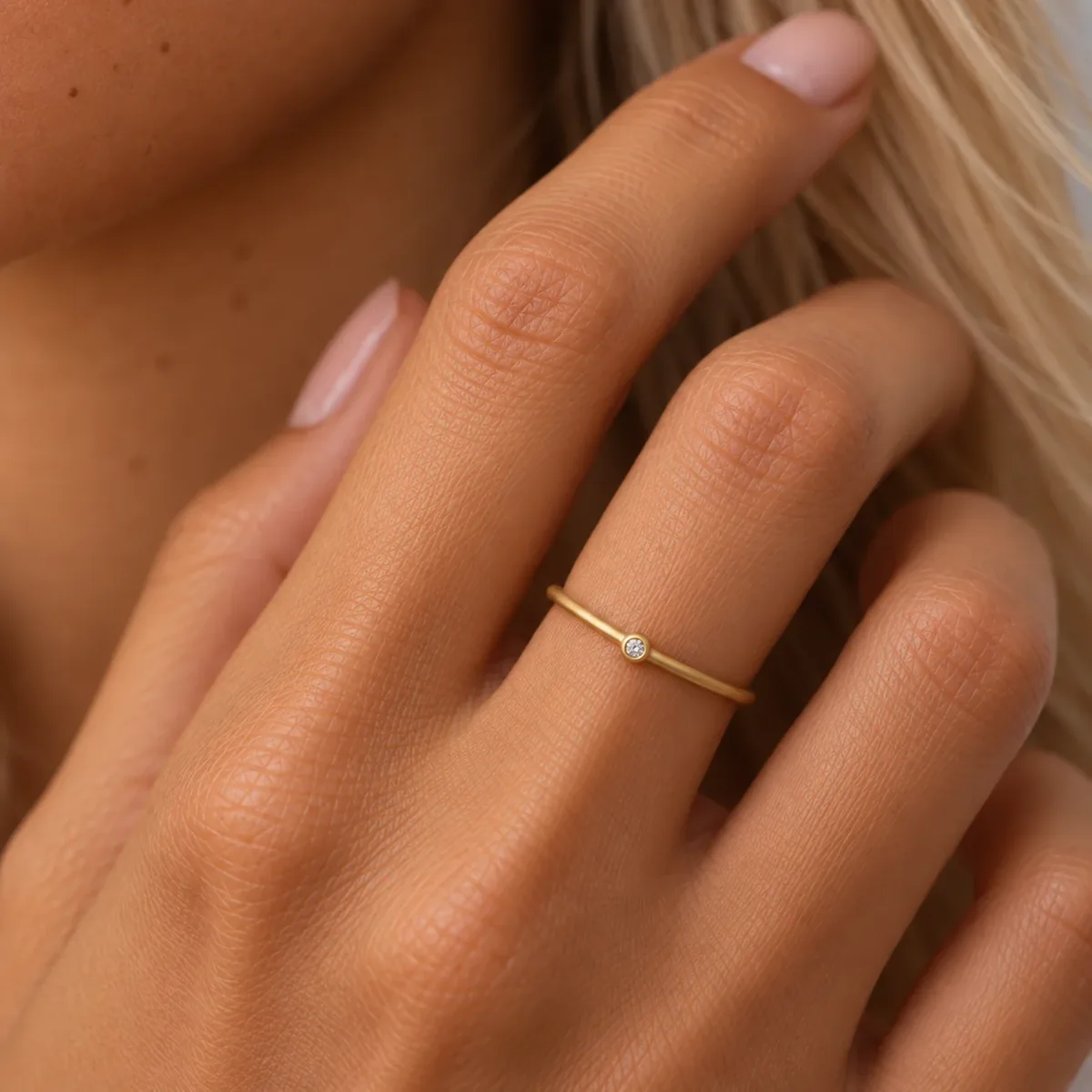Anillo fino de oro amarillo con pequeño diamante engastado en bisel, en la mano