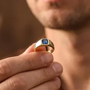 Hombre sujetando un anillo de oro con piedra azul cuadrada