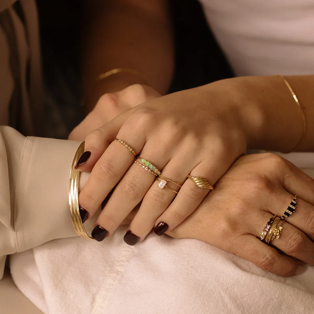 Mano de mujer con anillos de oro apilados con ópalos y circonitas