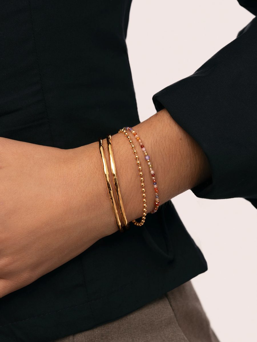 Dos brazaletes de oro martillados con pulseras finas de bolitas y piedras