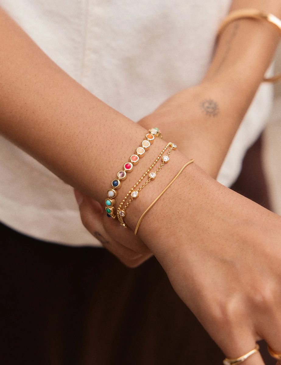 Pulsera de oro con piedras de colores engastadas, junto a pulseras finas