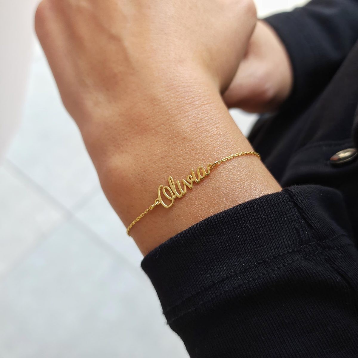 Pulsera de oro con un nombre en letras caligráficas puesta en la muñeca